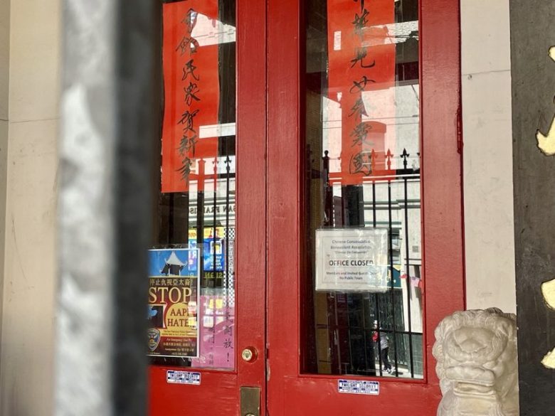 Red double doors with Chinese calligraphy banners, various notices, and a lion statue at the base. A sign on the door says "Office Closed".