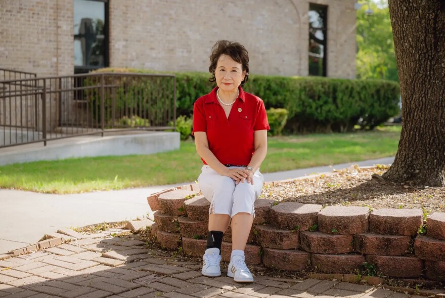 A woman sits outside on a wall of bricks next to a tree.