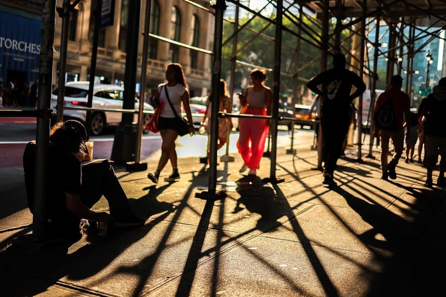 A homeless man sits on the ground as pedestrians walk by in a street of the Manhattan borough of New York on 5 August 2024. (Charly Triballeau/AFP)