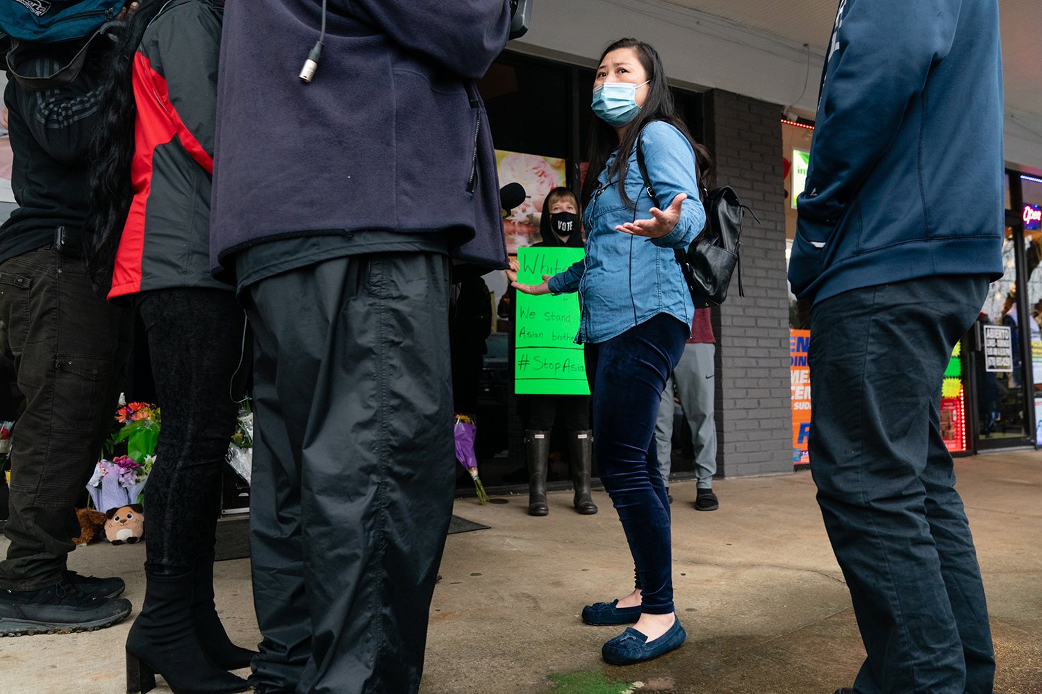 A woman wearing a mask gestures as she talks to the media around her.