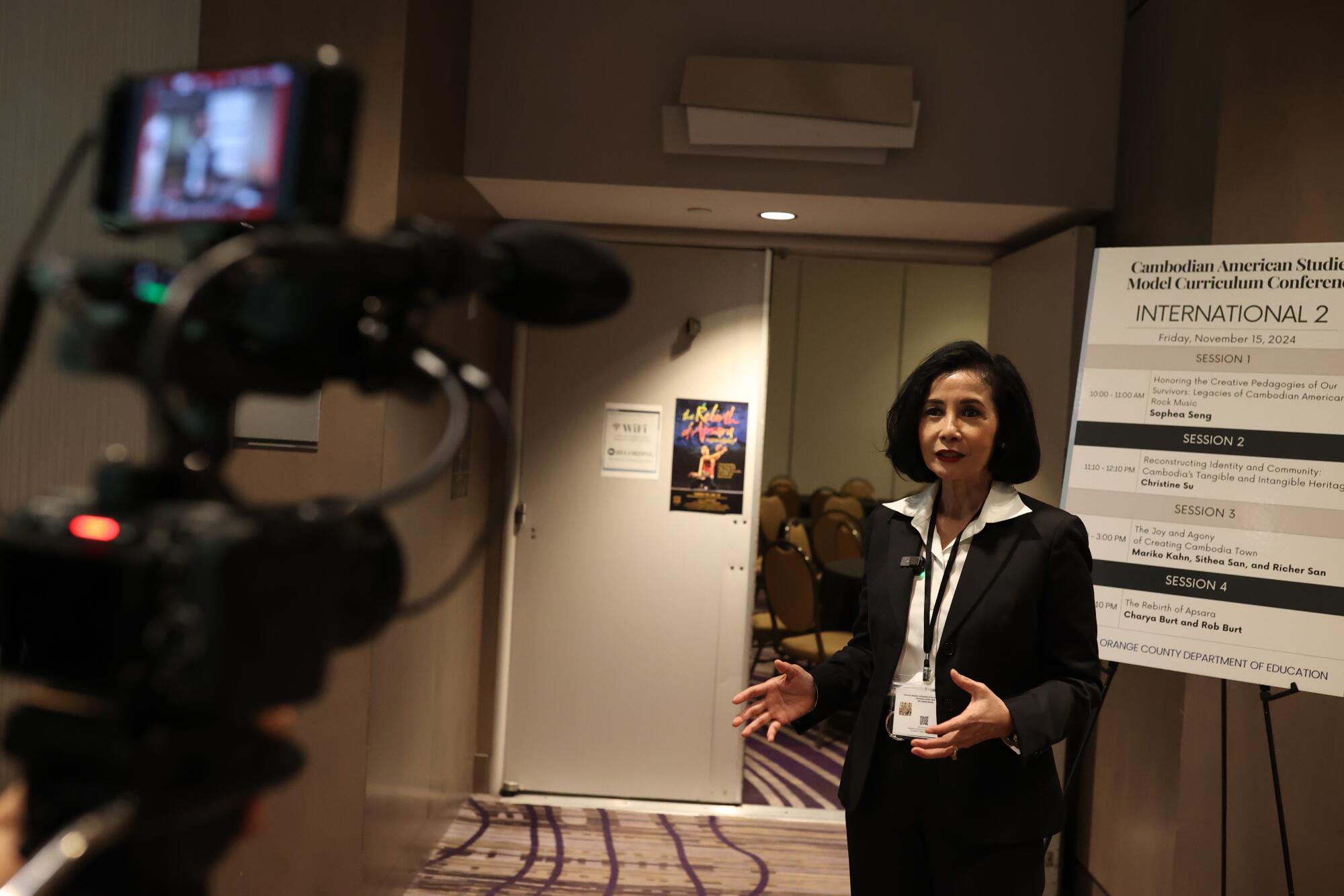 A camera records a person speaking beside an easel