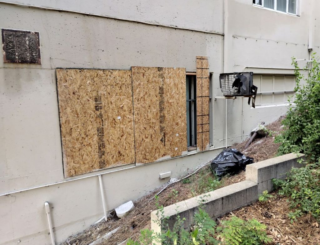 A trash bag near a boarded up window sits outside the grounds at the former Sakura  Intermediate Care Facility. 